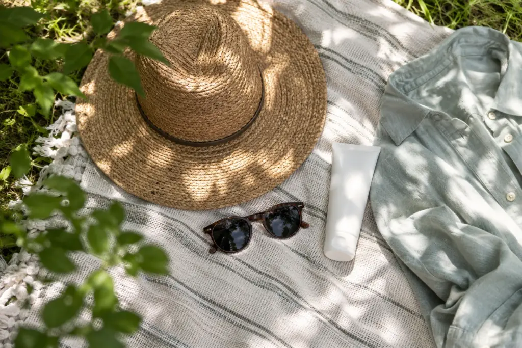 Sun hat, sunglasses, sunscreen and a light shirt in leafy shade